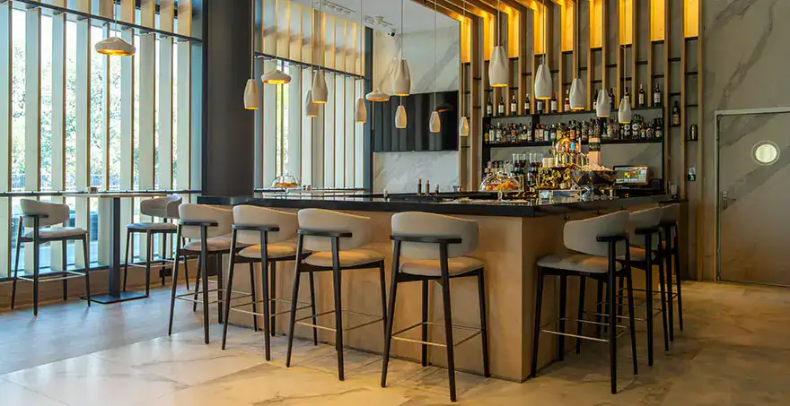 Moderno bar con sillas altas, luces colgantes y estanter&iacute;as llenas de botellas.