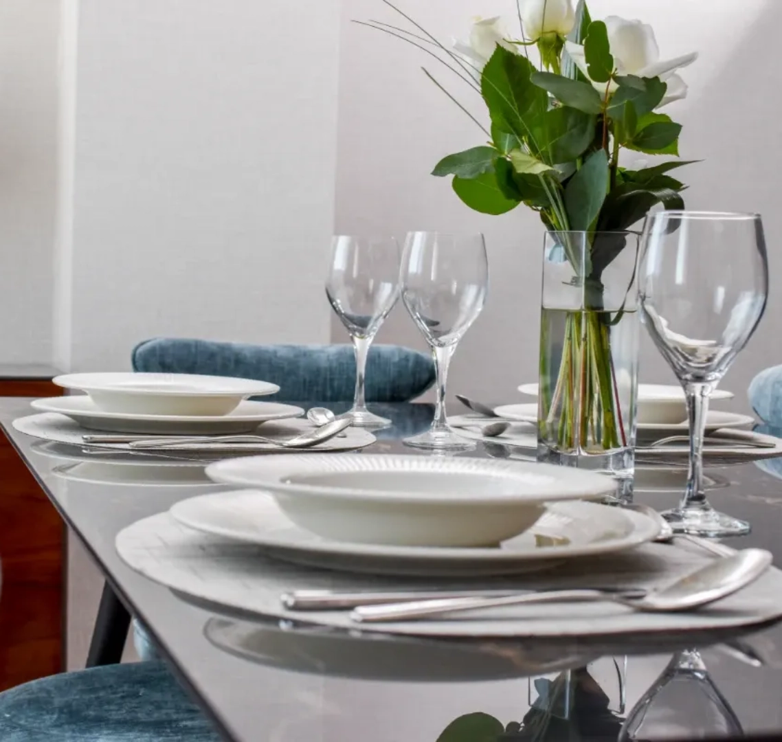 Mesa elegante con platos, copas y flores blancas en un jarr&oacute;n.