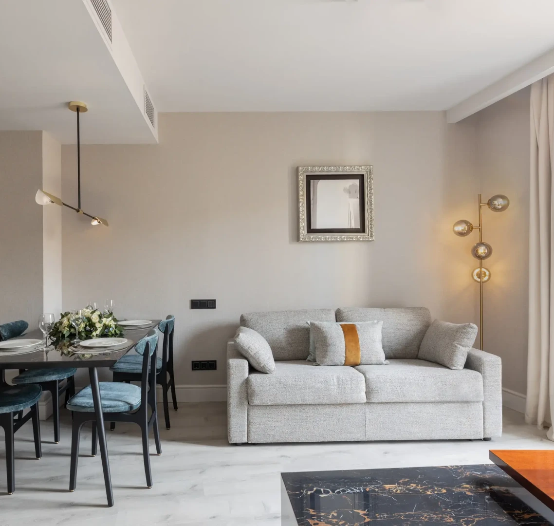 Sala moderna con sof&aacute; gris, mesa de comedor y l&aacute;mpara dorada.