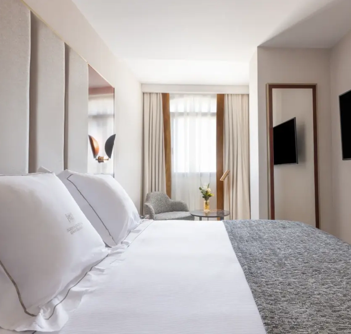 Habitaci&oacute;n de hotel moderna con cama doble y ventana al fondo.