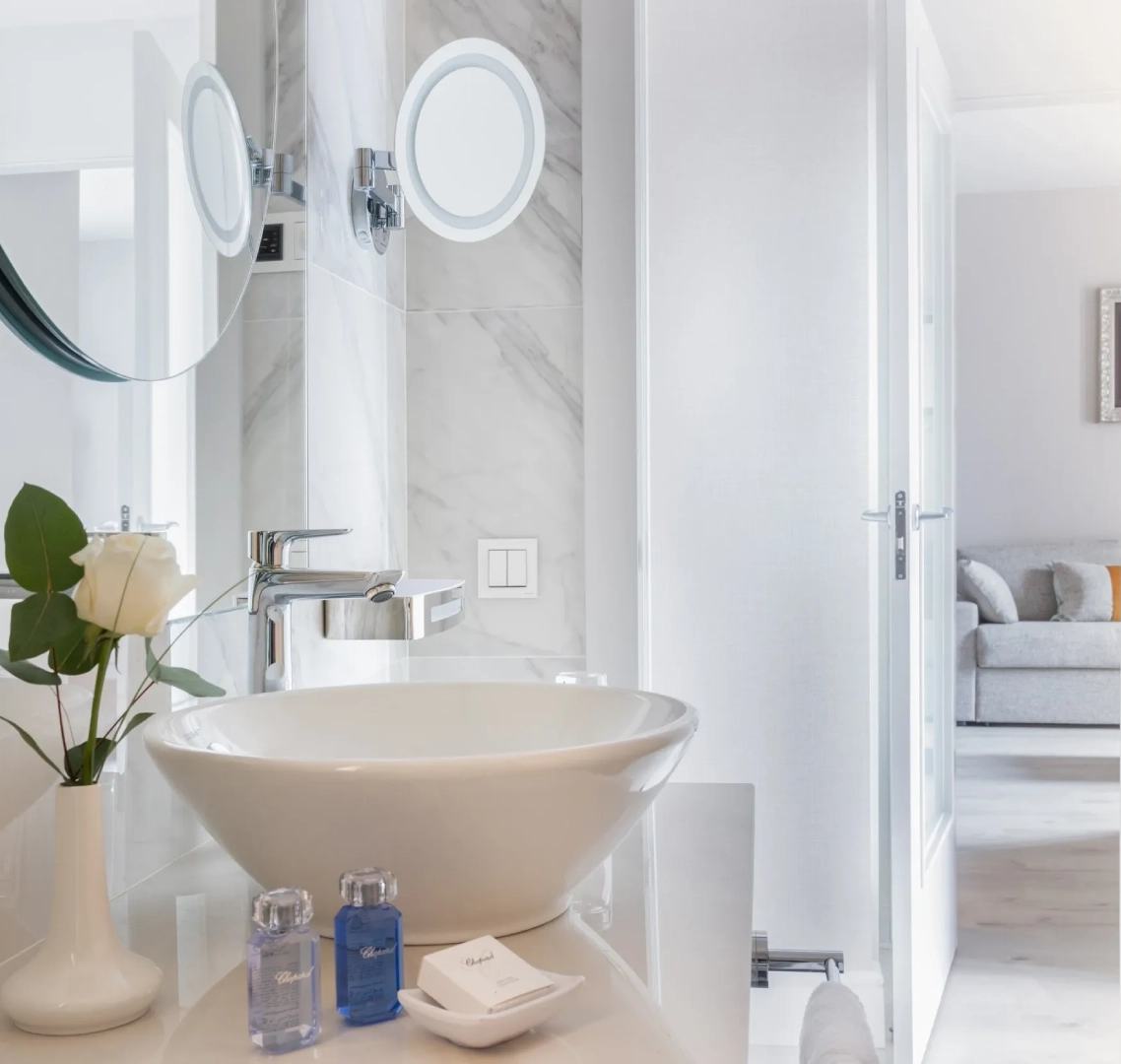 Ba&ntilde;o moderno con lavabo blanco, espejo circular y accesorios de tocador.