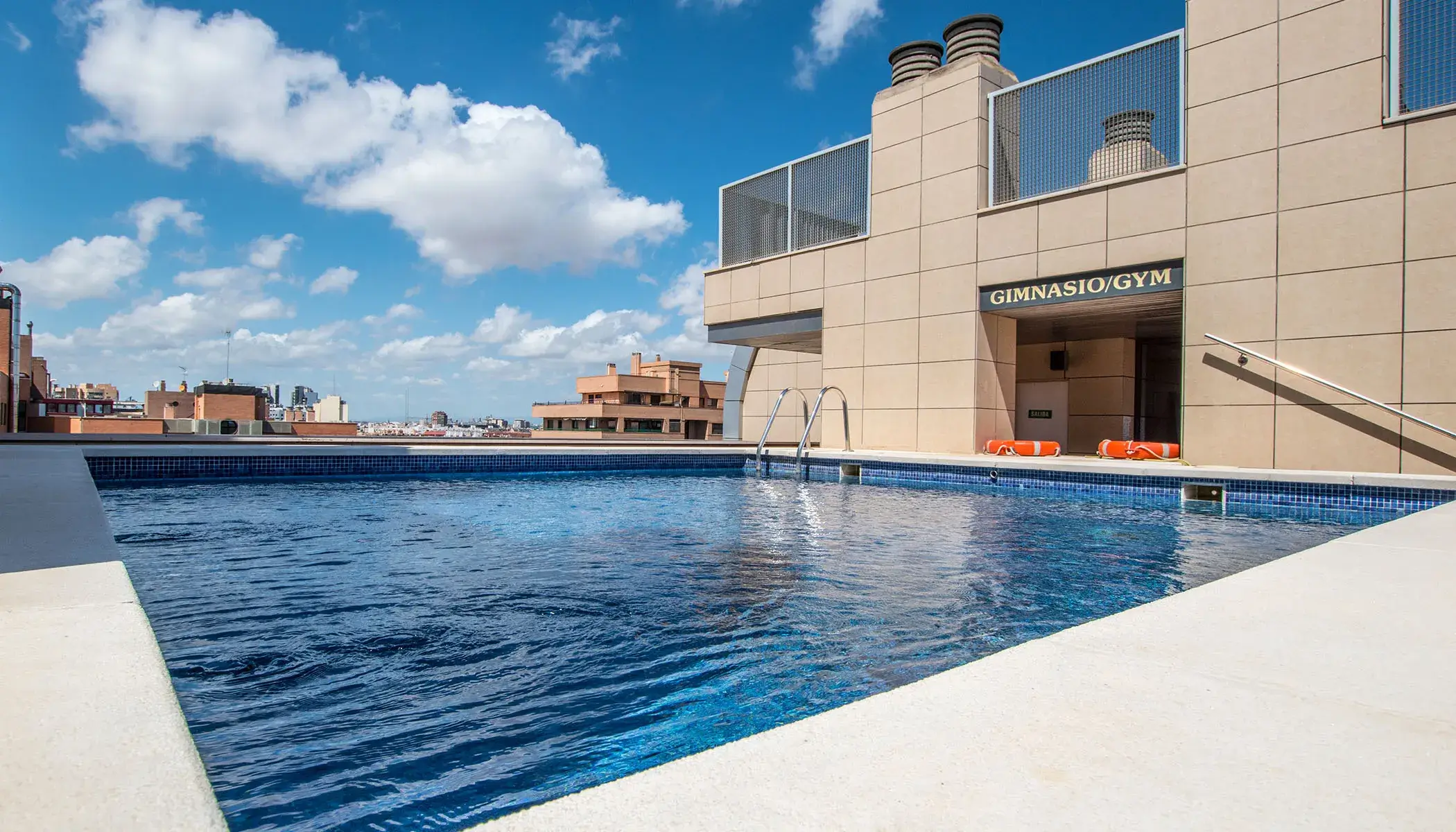 Piscina en una azotea junto a un gimnasio, d&iacute;a soleado con nubes.