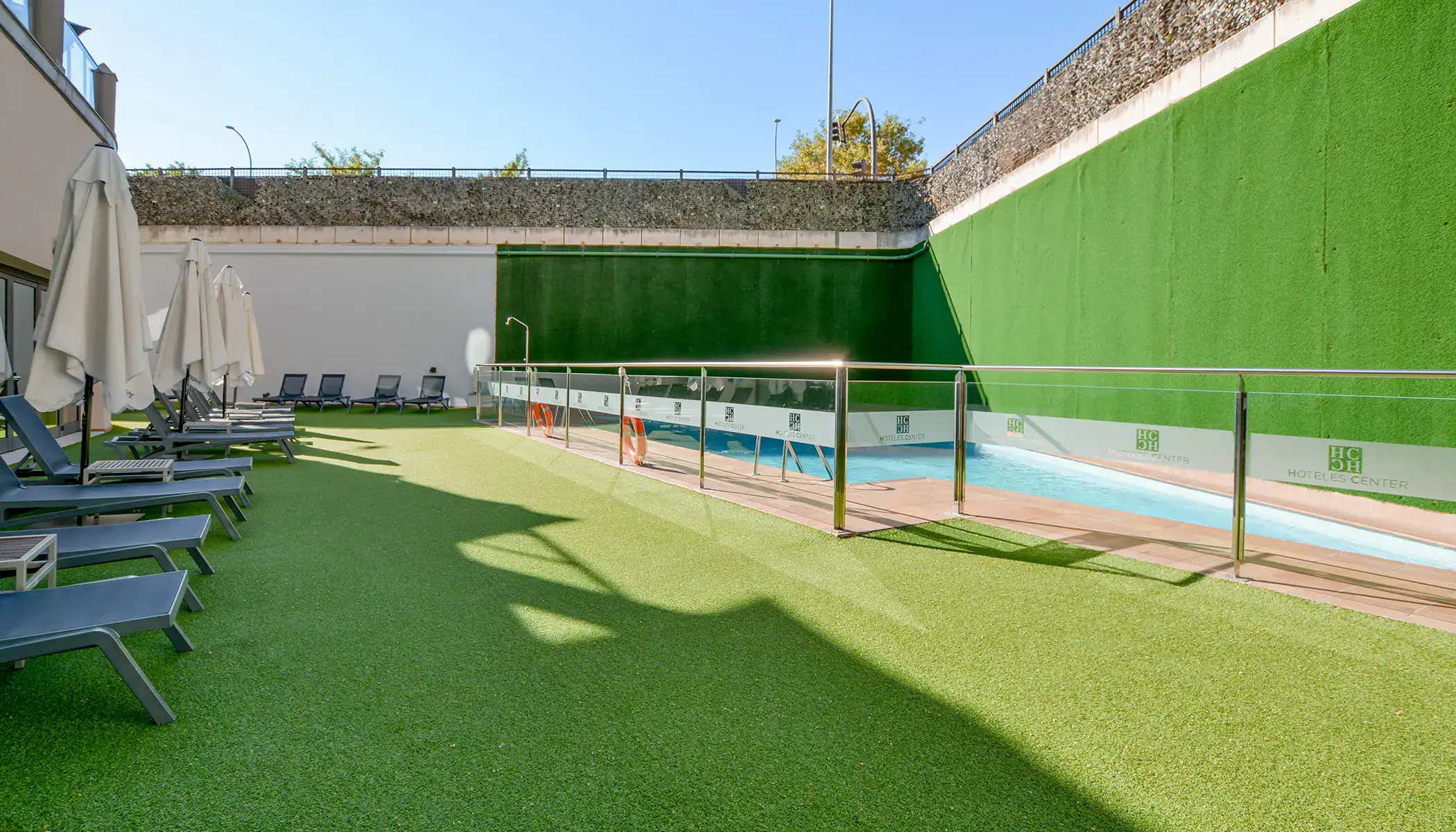 Piscina al aire libre con tumbonas y sombrillas en un &aacute;rea con c&eacute;sped artificial.