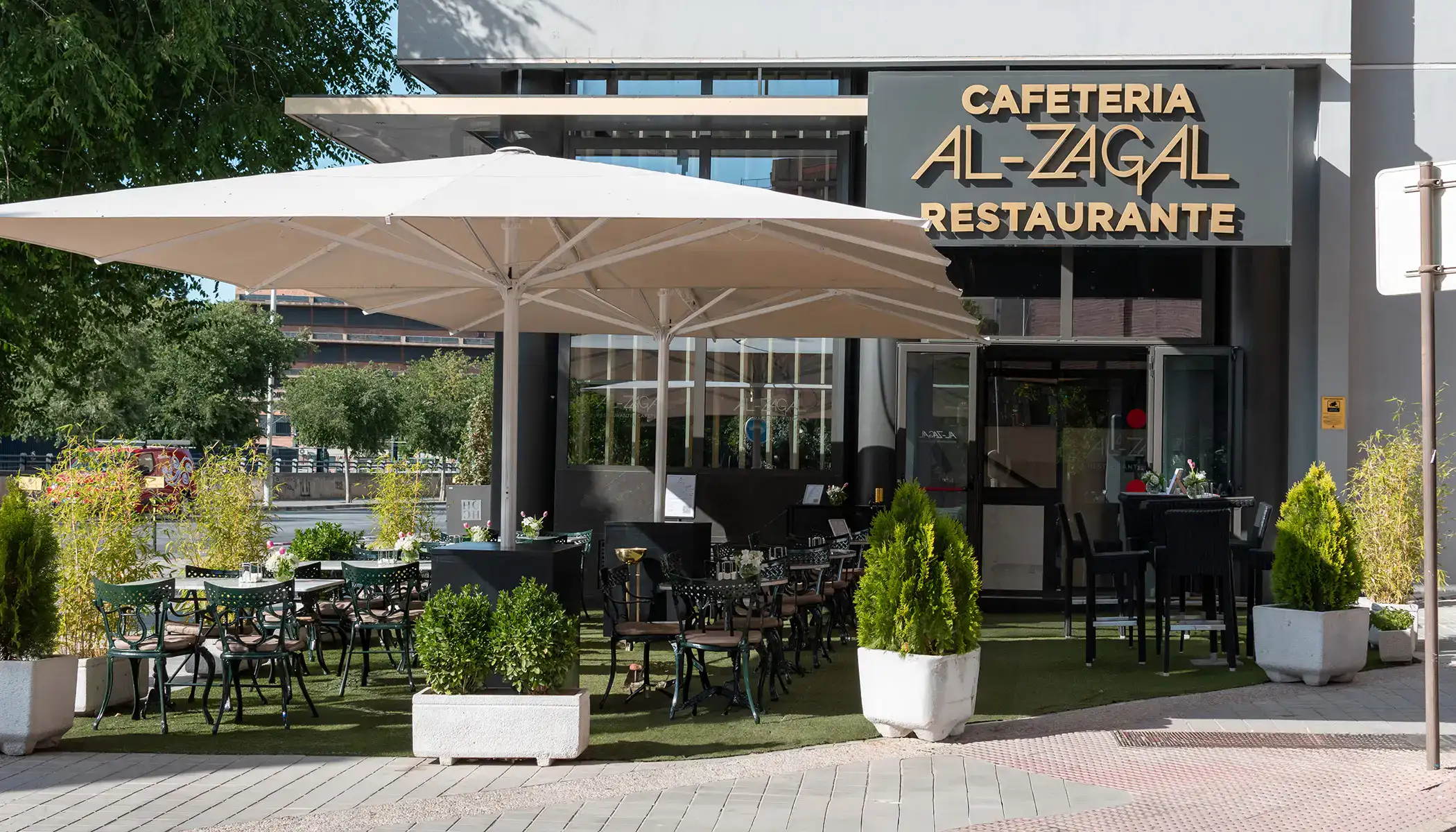 Exterior de una cafeter&iacute;a con mesas al aire libre bajo sombrillas grandes.