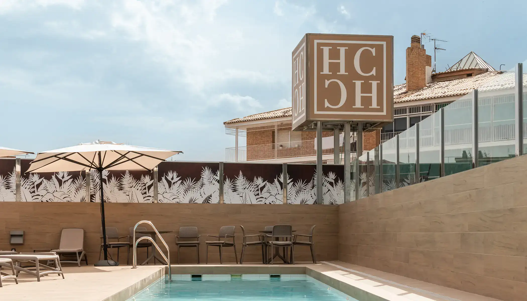 Piscina con tumbonas, sombrilla y letrero de un hotel.