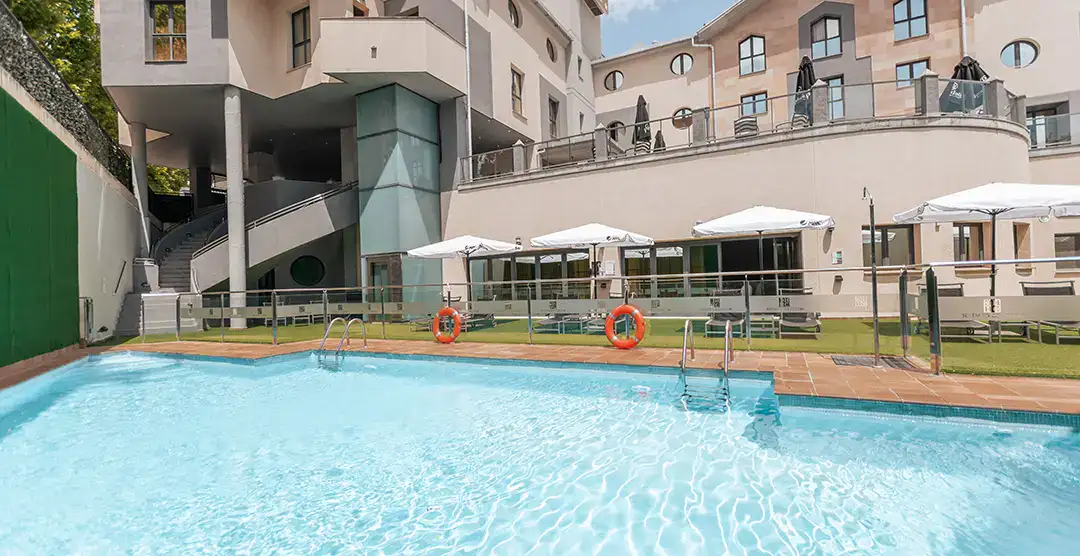Piscina al aire libre junto a un edificio moderno y sombrillas blancas.