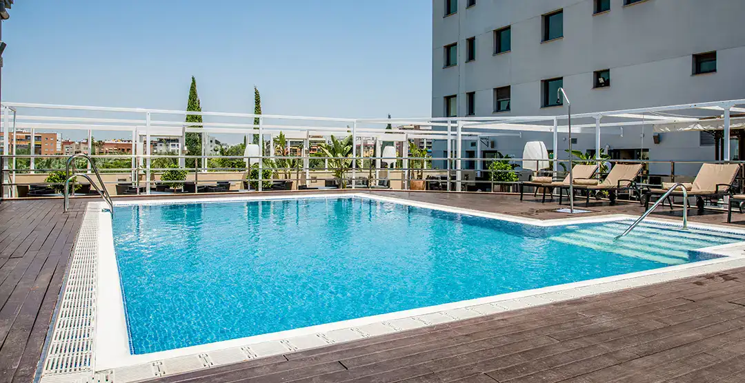 Piscina en la terraza de un edificio con tumbonas y cielo despejado.