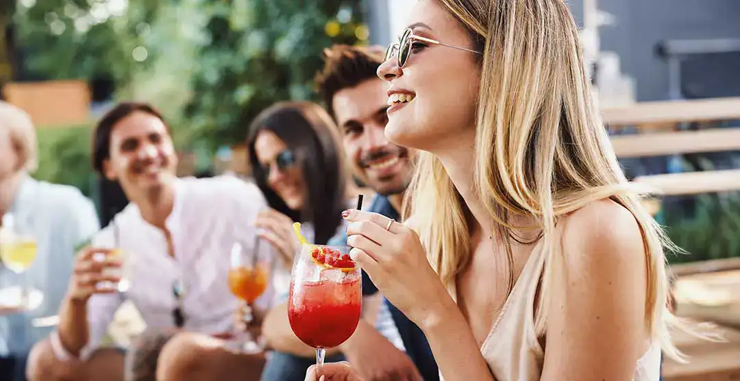 Grupo de amigos sonriendo y disfrutando bebidas al aire libre.