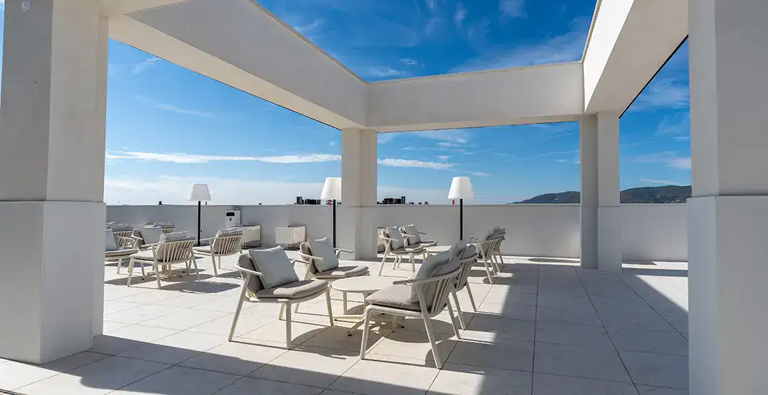 Terraza moderna con mesas y sillas blancas bajo un cielo azul despejado.