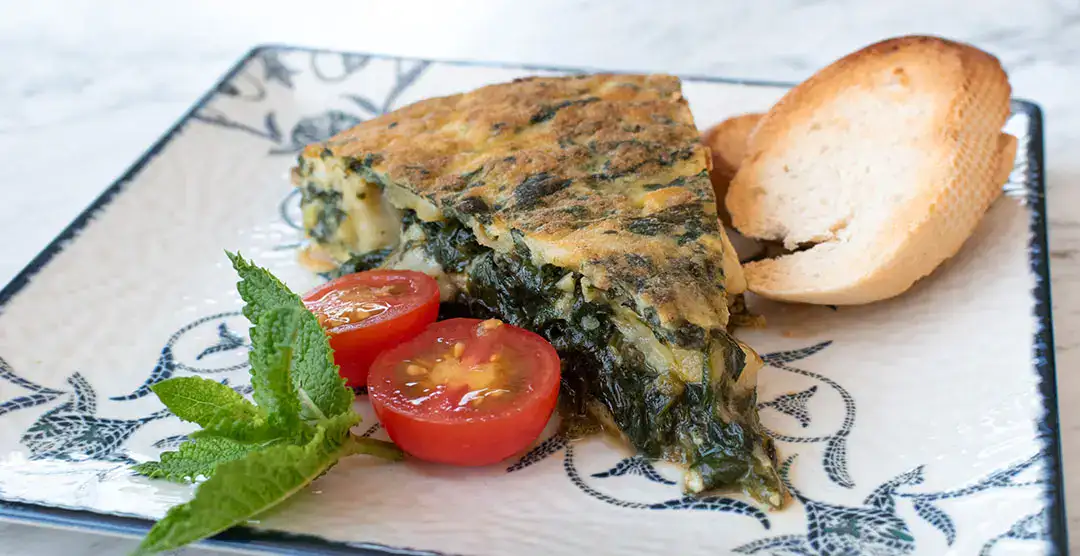 Tortilla de espinacas, tomate cherry, menta y pan en un plato decorado.