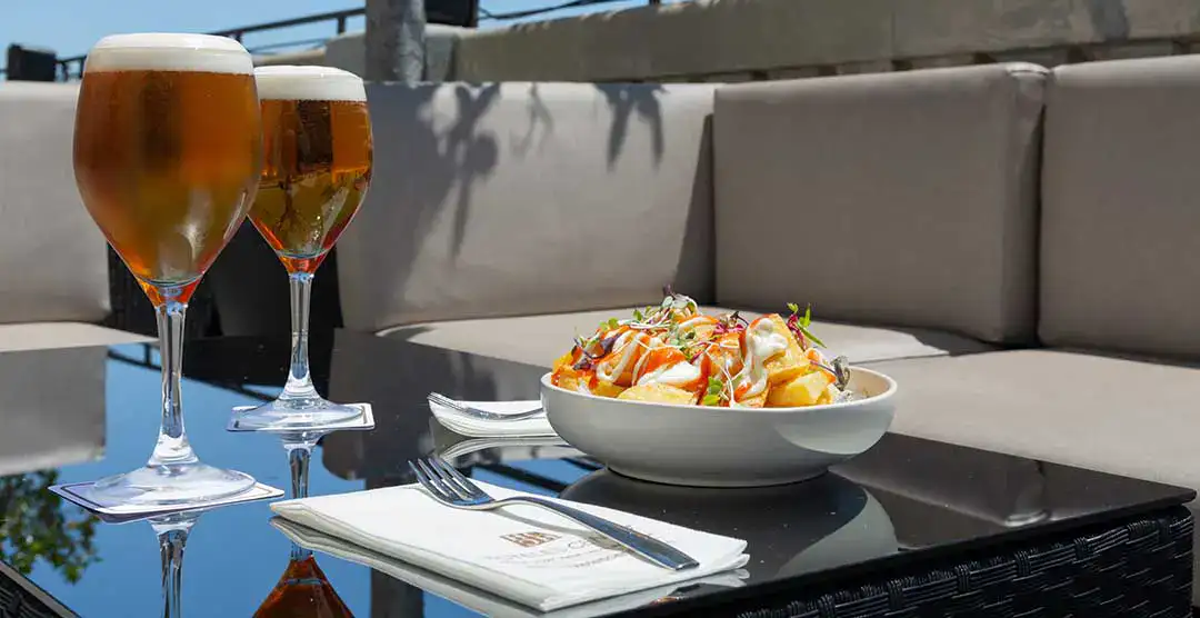 Dos cervezas y patatas bravas en una mesa al aire libre.
