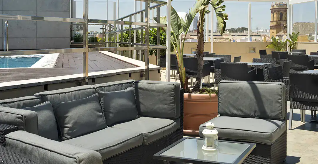 Terraza con sof&aacute;s grises, piscina y vistas de la ciudad al fondo.