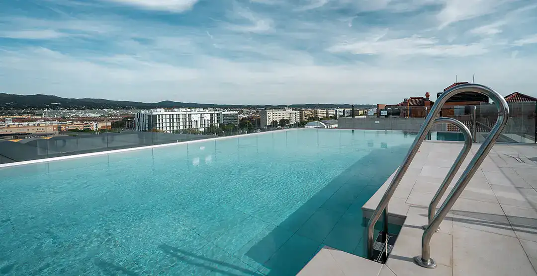 Piscina infinita en azotea con vista a la ciudad y monta&ntilde;as al fondo.