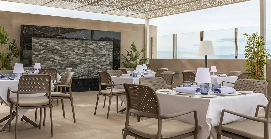 Terraza elegante con mesas y sillas bajo un techo decorativo y plantas alrededor.