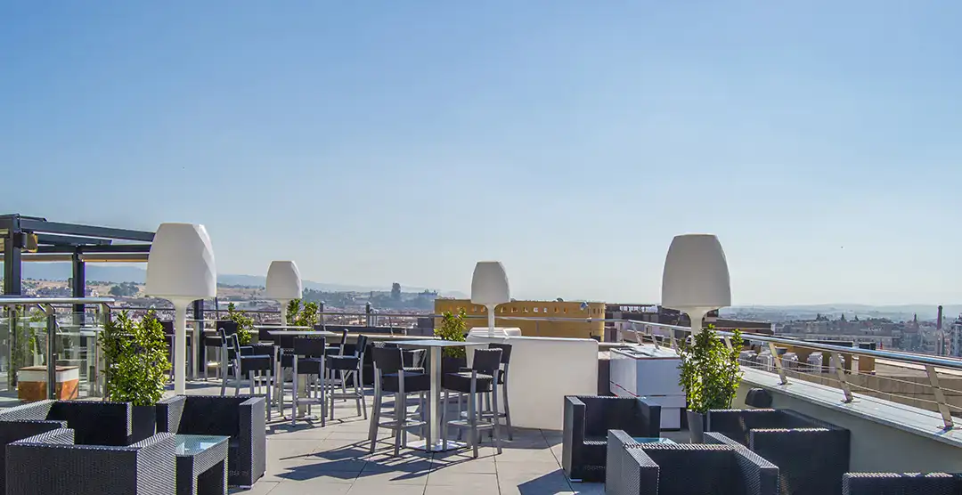 Terraza al aire libre con mesas, sillas y l&aacute;mparas modernas bajo un cielo despejado.