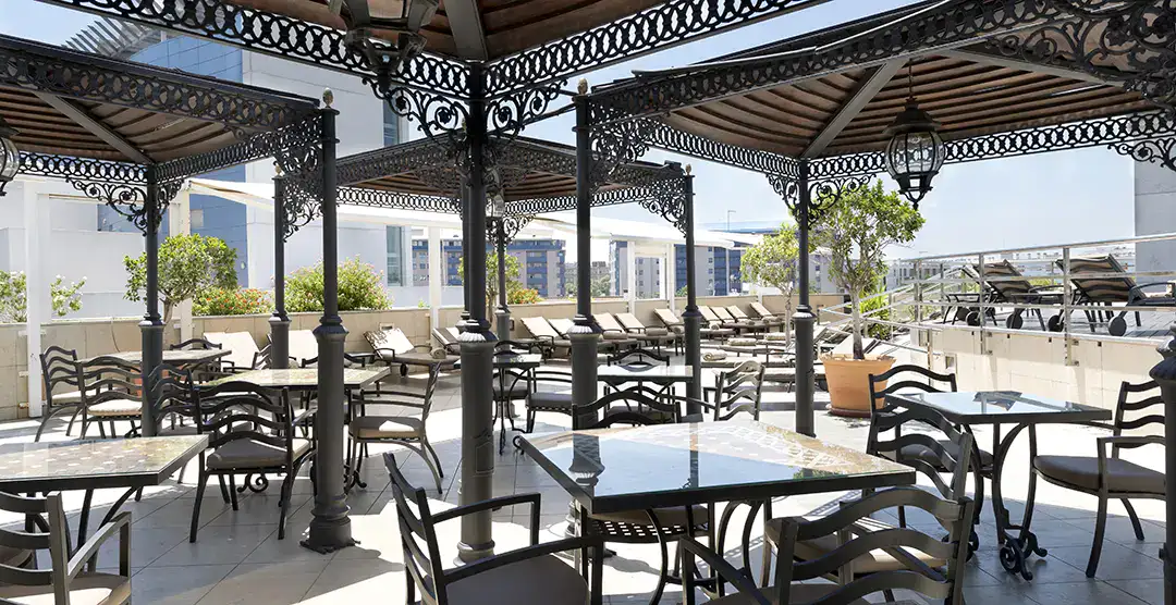 Terraza con mesas y sillas bajo p&eacute;rgolas decorativas al aire libre.