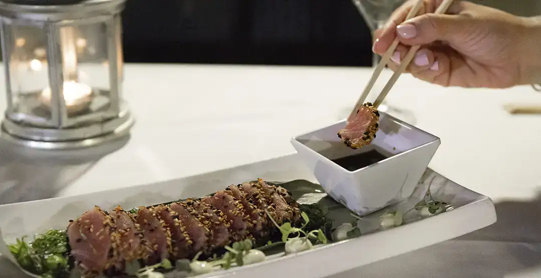 Plato de at&uacute;n sellado, salsa de soya y linterna decorativa al fondo.