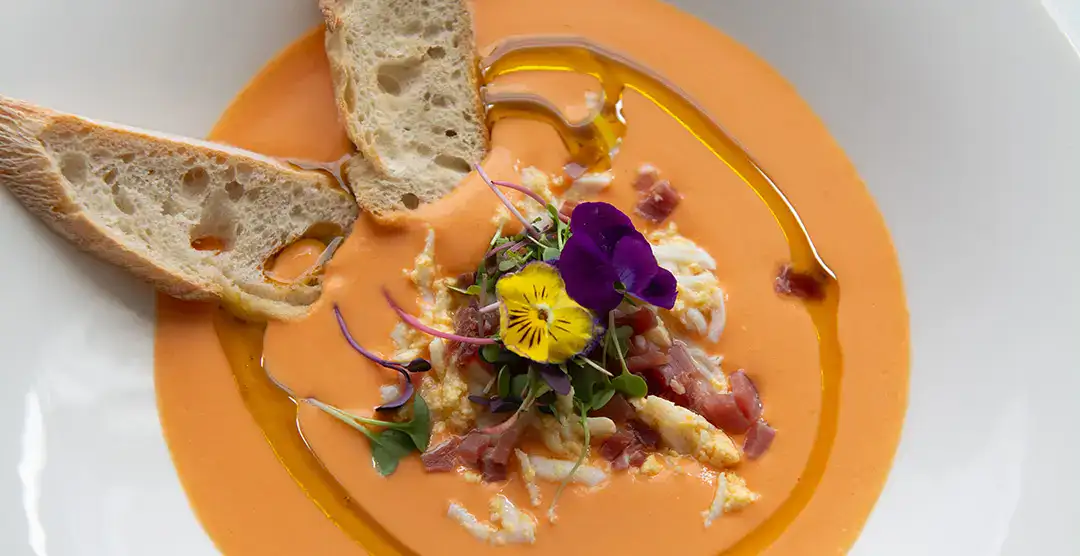Plato de salmorejo con huevo, jam&oacute;n, flores y pan crujiente.