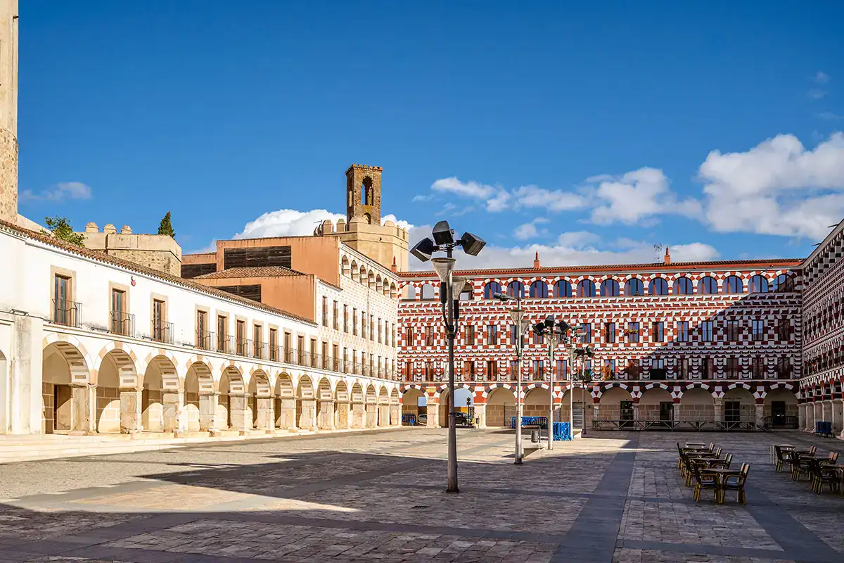 Plaza con edificios de arcos y fachada decorativa bajo un cielo azul.