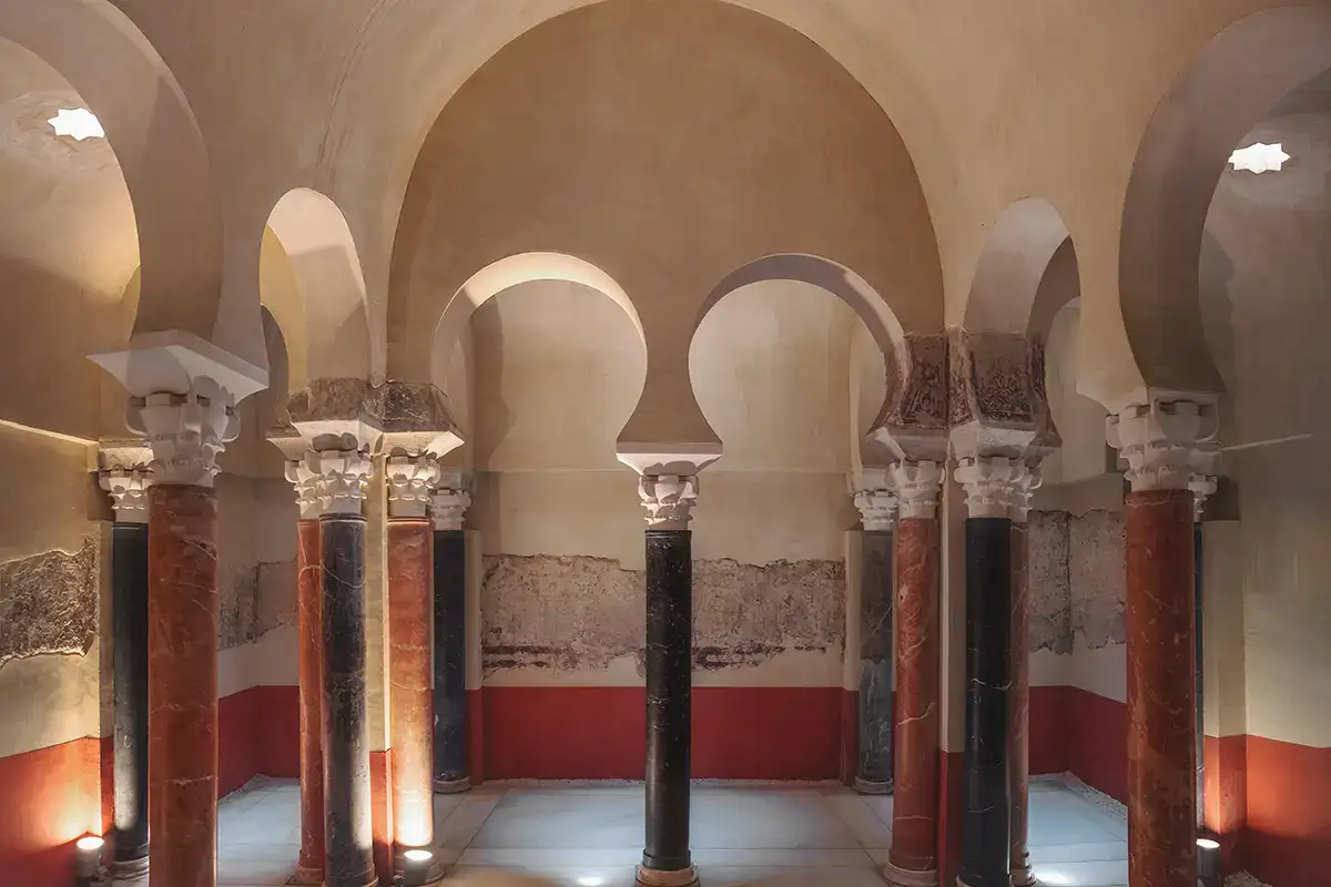Sala con columnas y arcos de herradura, iluminaci&oacute;n c&aacute;lida y paredes decoradas.