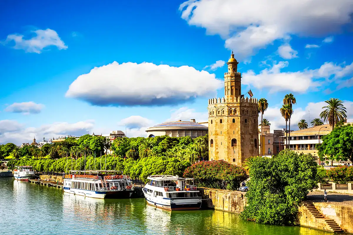 Torre junto al r&iacute;o con barcos y un cielo azul con nubes.