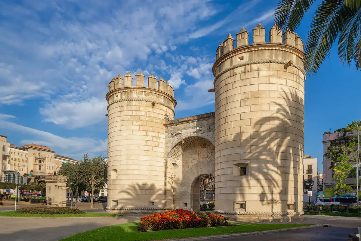 Torres de piedra con una sombra de palmera sobre ellas, cielo parcialmente nublado.