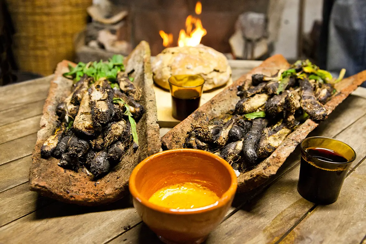 Platillos de cal&ccedil;ots asados con salsa y vino sobre una mesa r&uacute;stica.