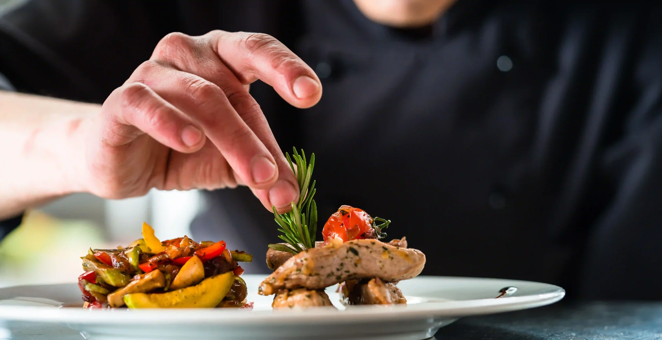 Chef decorando un plato con carne y verduras asadas.