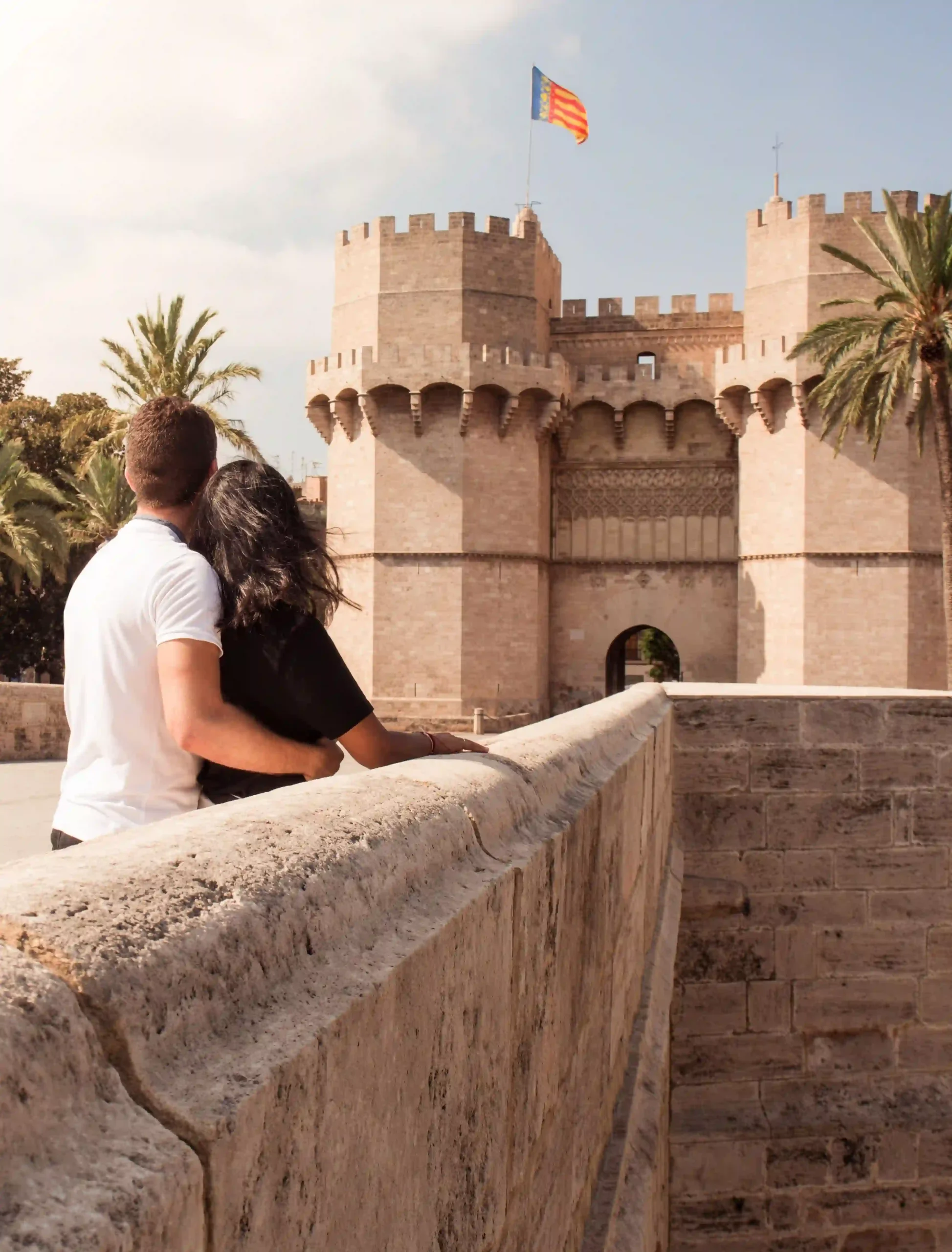 Pareja mirando una antigua torre con bandera y palmeras alrededor.