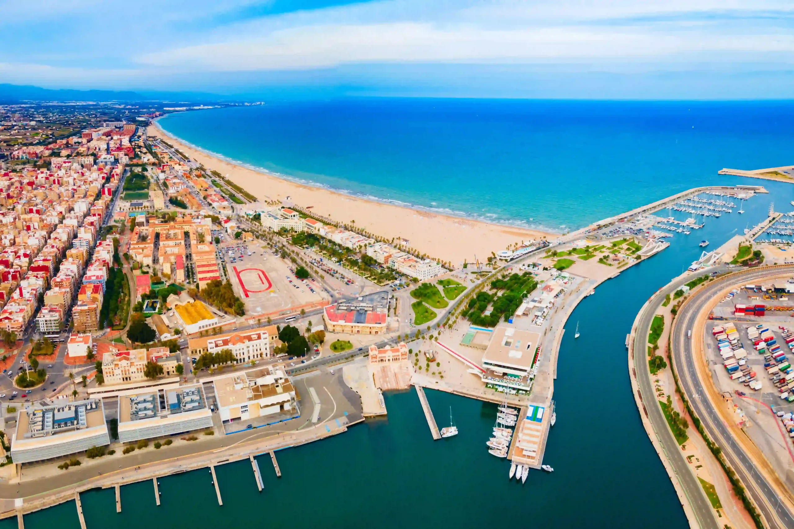 Vista a&eacute;rea de una ciudad costera con playa, puerto y edificios cercanos al mar.