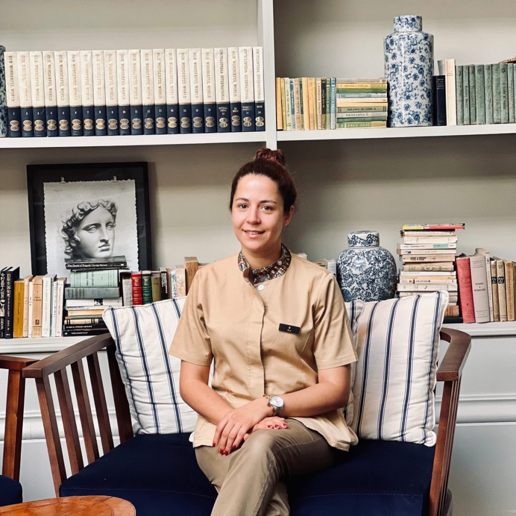 Person sitting on a cushioned couch with books and vases on a shelf behind them.