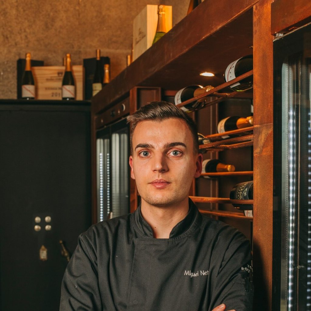 Chef in black uniform standing in a wine cellar.