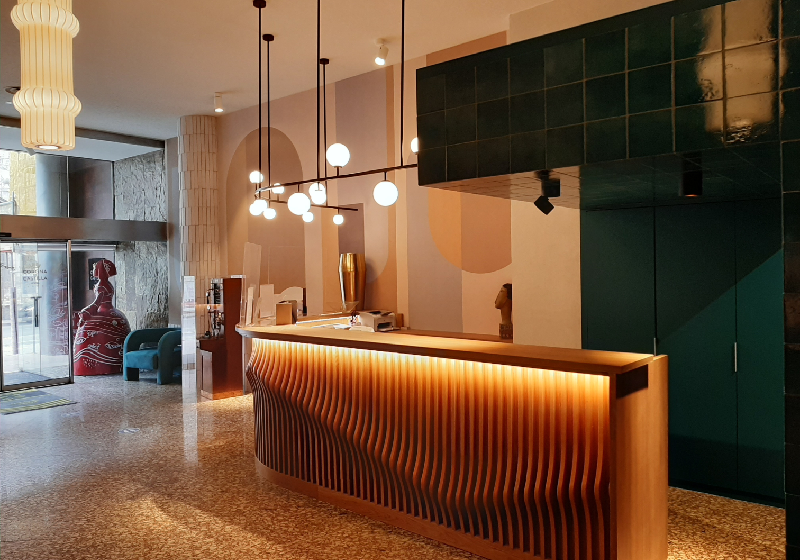 Vestíbulo de hotel moderno con mostrador de recepción iluminado, lámparas colgantes y decoración contemporánea.