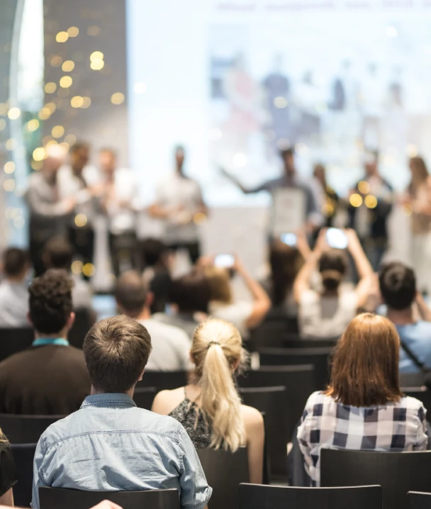 Personas asistiendo a una conferencia, varias grabando con sus tel&eacute;fonos.