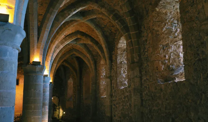Pasillo de castillo medieval con arcos de piedra iluminado suavemente.
