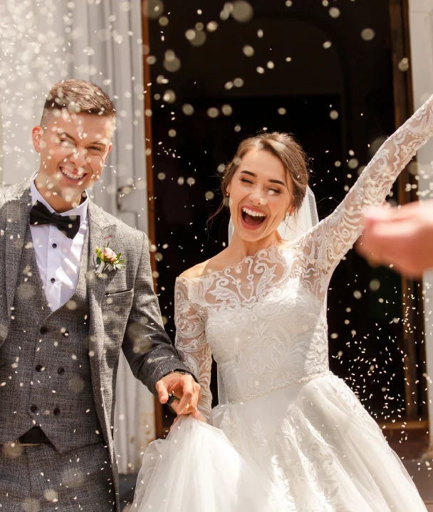 Pareja de reci&eacute;n casados sonr&iacute;e bajo una lluvia de confeti a la salida de la iglesia.