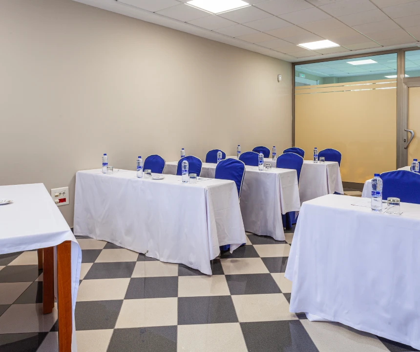Sala de reuniones con mesas cubiertas y sillas azules, preparada para una conferencia.