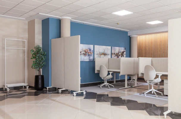 Oficina moderna con cub&iacute;culos, sillas giratorias y decoraci&oacute;n minimalista en azul y beige.