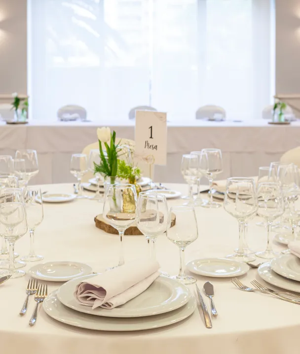 Mesa de banquete con copas, vajilla blanca, servilletas y centro de mesa floral elegante.