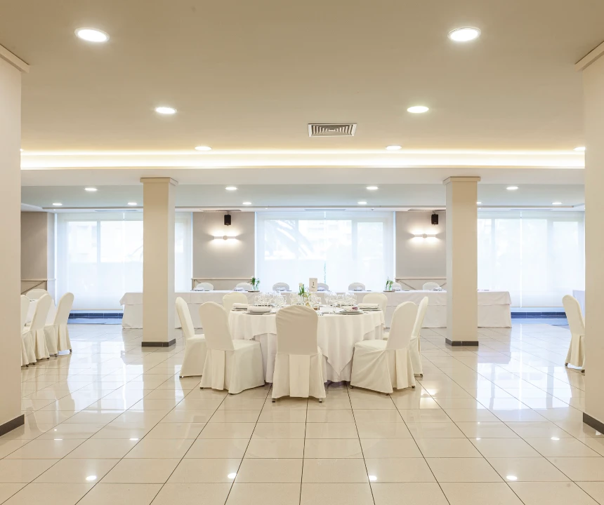 Sal&oacute;n de banquetes elegante con mesa redonda, sillas blancas y decoraci&oacute;n minimalista.