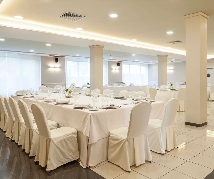 Sala de banquete con mesas blancas, sillas y copas listas para un evento formal.