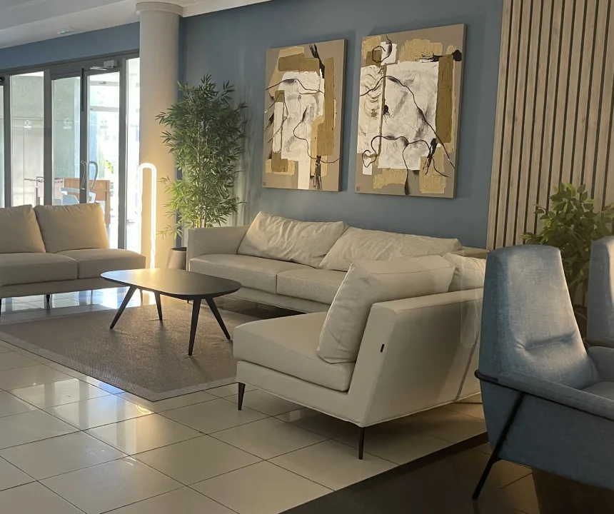 Sala moderna con sofás beige, mesas negras, arte abstracto y plantas decorativas.