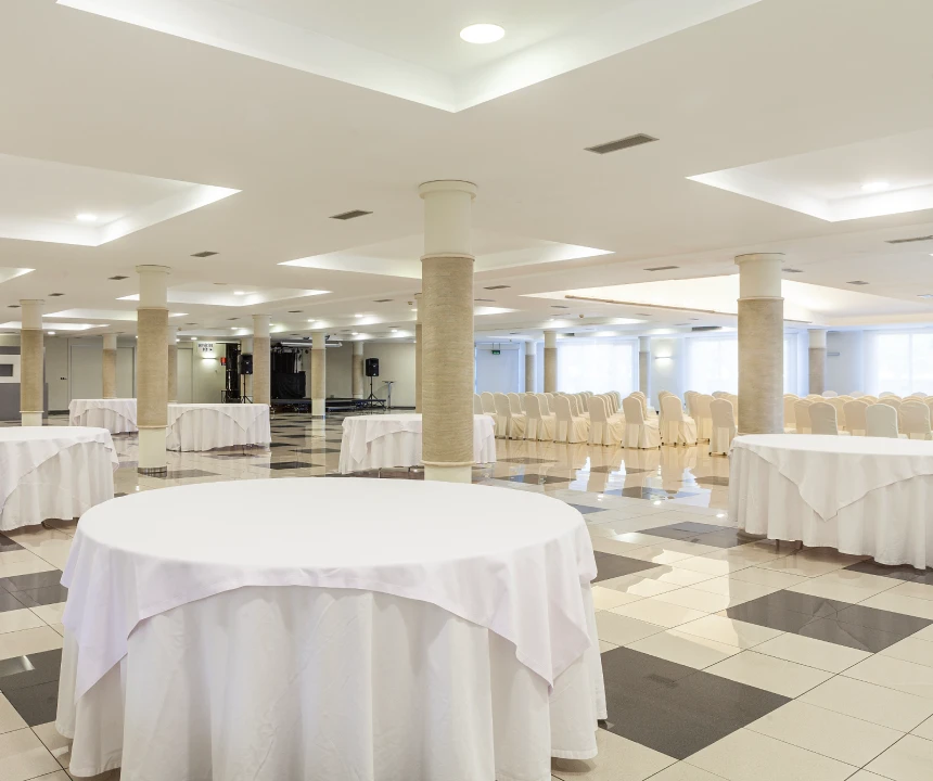 Sala de eventos elegante con mesas redondas y sillas alineadas, iluminada suavemente.