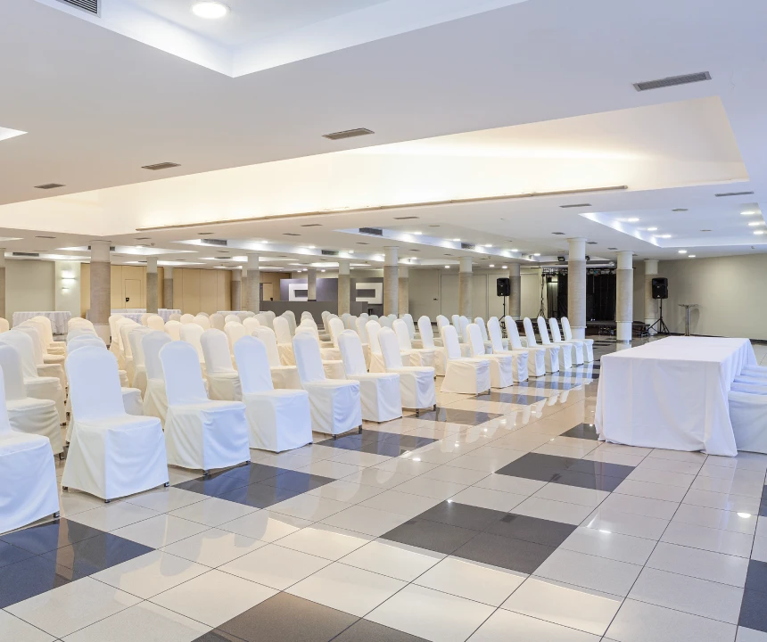 Sala de conferencias con sillas blancas y mesa cubierta, suelo de cuadros.