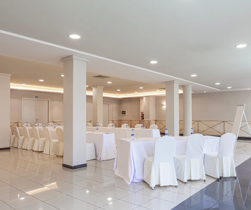 Sala de conferencias con mesas en forma de U, sillas blancas y un rotafolio al fondo.