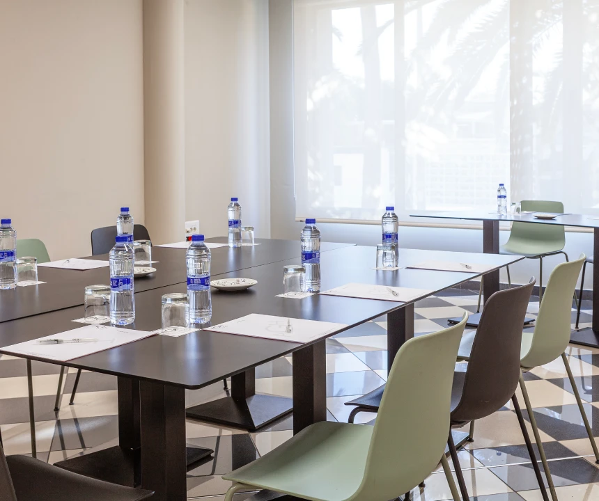 Sala de reuniones con mesas dispuestas en cuadrado, sillas, agua y papeler&iacute;a.