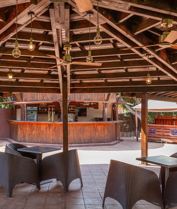 &Aacute;rea de bar al aire libre, techada, con sillas de mimbre y mostrador de madera.