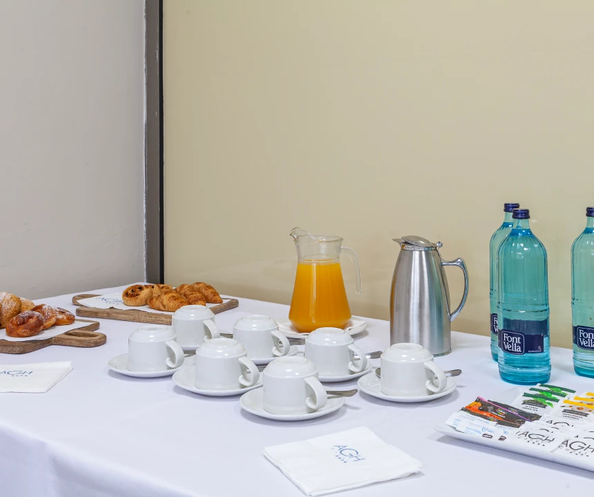 Mesa con tazas, agua, caf&eacute;, jugo de naranja y bandejas de croissants.