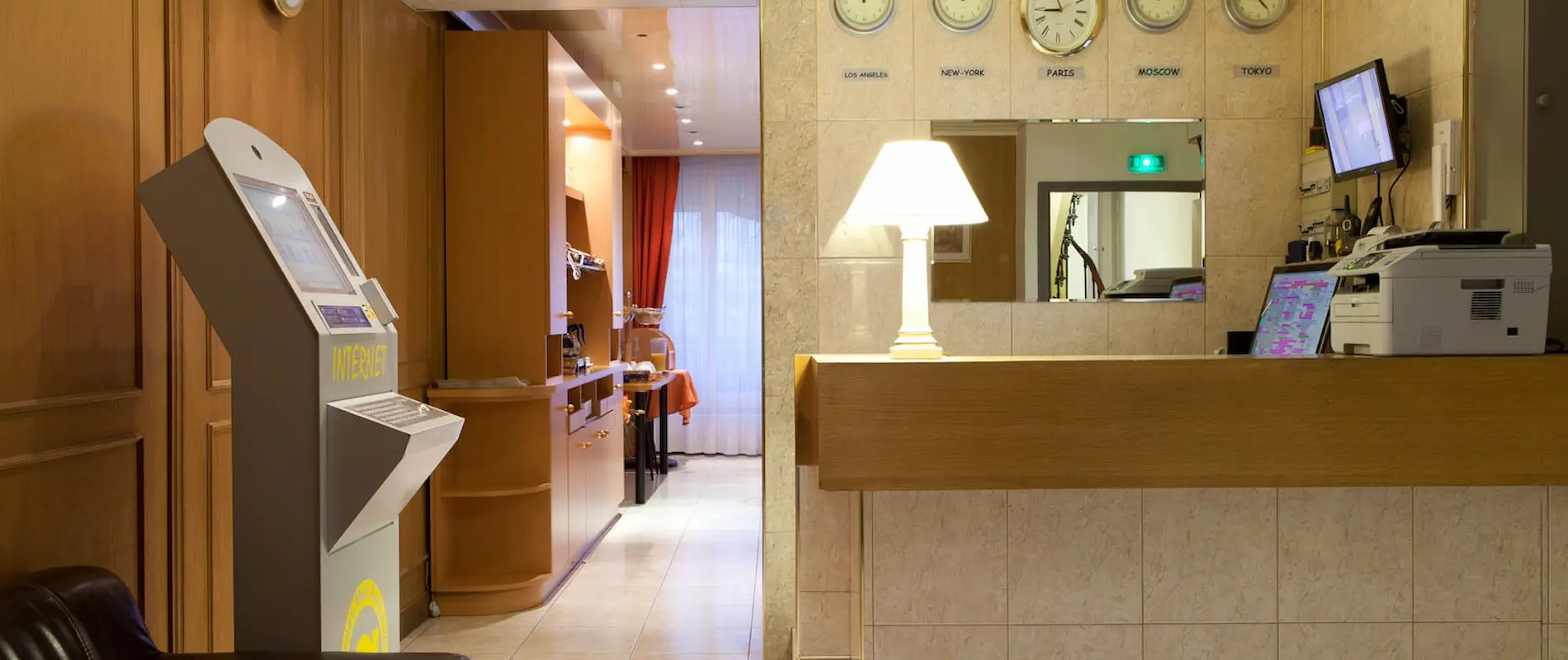Réception d’hôtel avec horloges mondiales, lumière tamisée et borne internet.