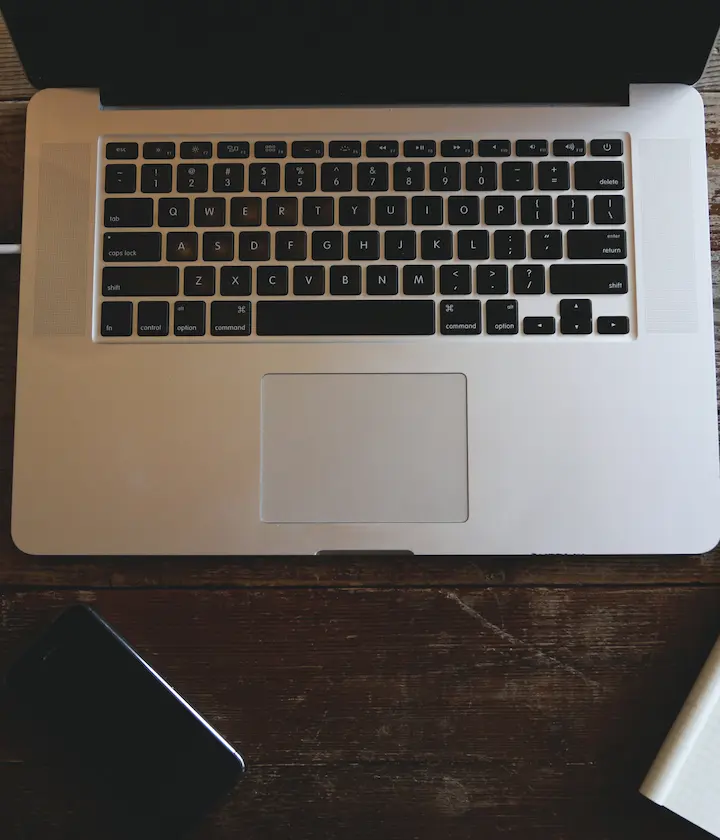Clavier d'ordinateur portable sur une table en bois, téléphone et carnet à proximité.